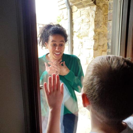 A teacher interacting with a student through the glass of their front door during pandamic.